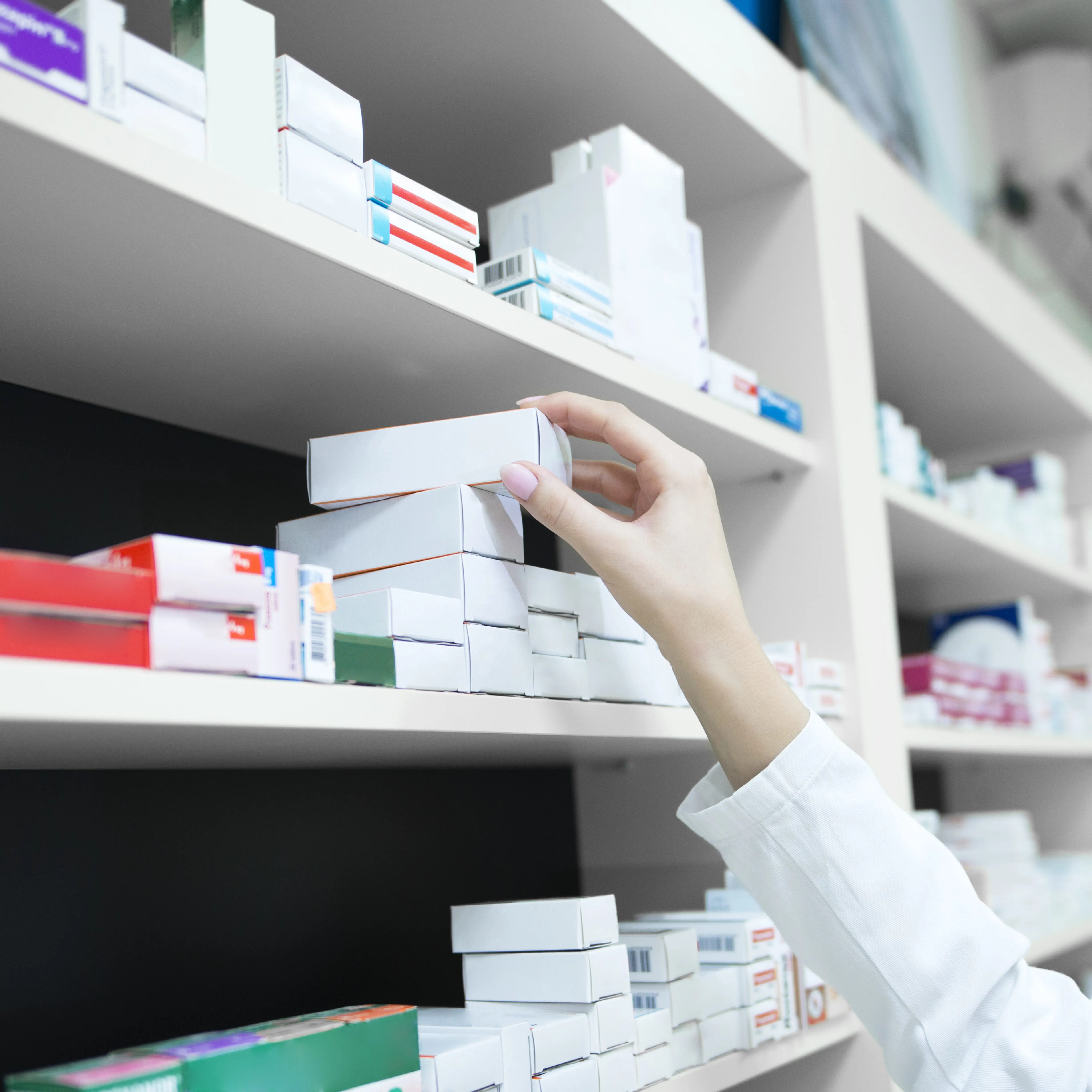 Closeup view of pharmacist hand taking medicine box from the shelf in drug store.